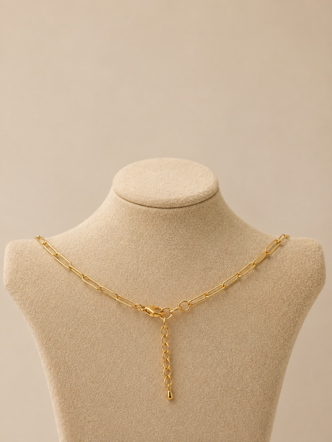 Gold paperclip necklace with lobster clasp and extender chain on a nude background