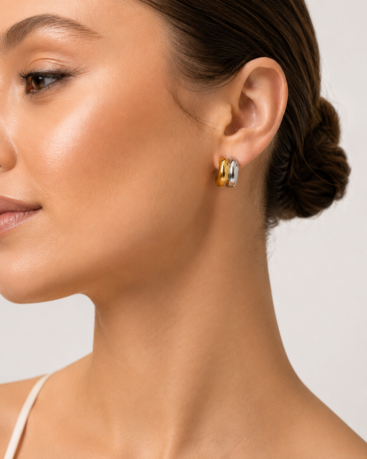 A close-up side profile of a woman wearing a pair of small hoop earrings with alternating gold and silver-toned metal bands, Duet Luxe two-tone sculpted hoop earrings worn by model