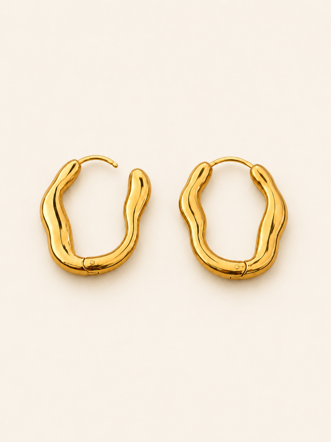 A pair of gold-toned, wavy open hoop earrings on a clean, solid off-white background.