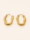 A pair of gold-toned, wavy open hoop earrings on a clean, solid off-white background.