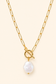 A gold chain necklace featuring a toggle clasp and a dangling baroque pearl pendant, displayed on a solid cream background.