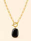 A gold paperclip chain necklace with a toggle clasp and a polished black stone pendant, shown against a solid light beige background.