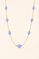 A gold chain necklace featuring seven light blue round beads spaced along the chain, displayed against a solid pale beige background.