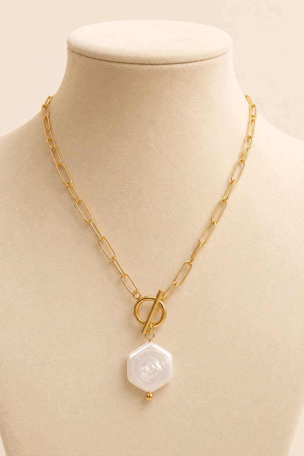 Celeste gold paperclip toggle necklace with pearl pendant displayed on cream mannequin