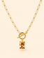 A gold paperclip chain necklace with a toggle clasp and a rectangular amber gemstone pendant, shown against a solid pale peach background.