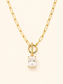 A gold paperclip chain necklace with a toggle clasp and a rectangular clear gemstone pendant, shown on a light cream background.