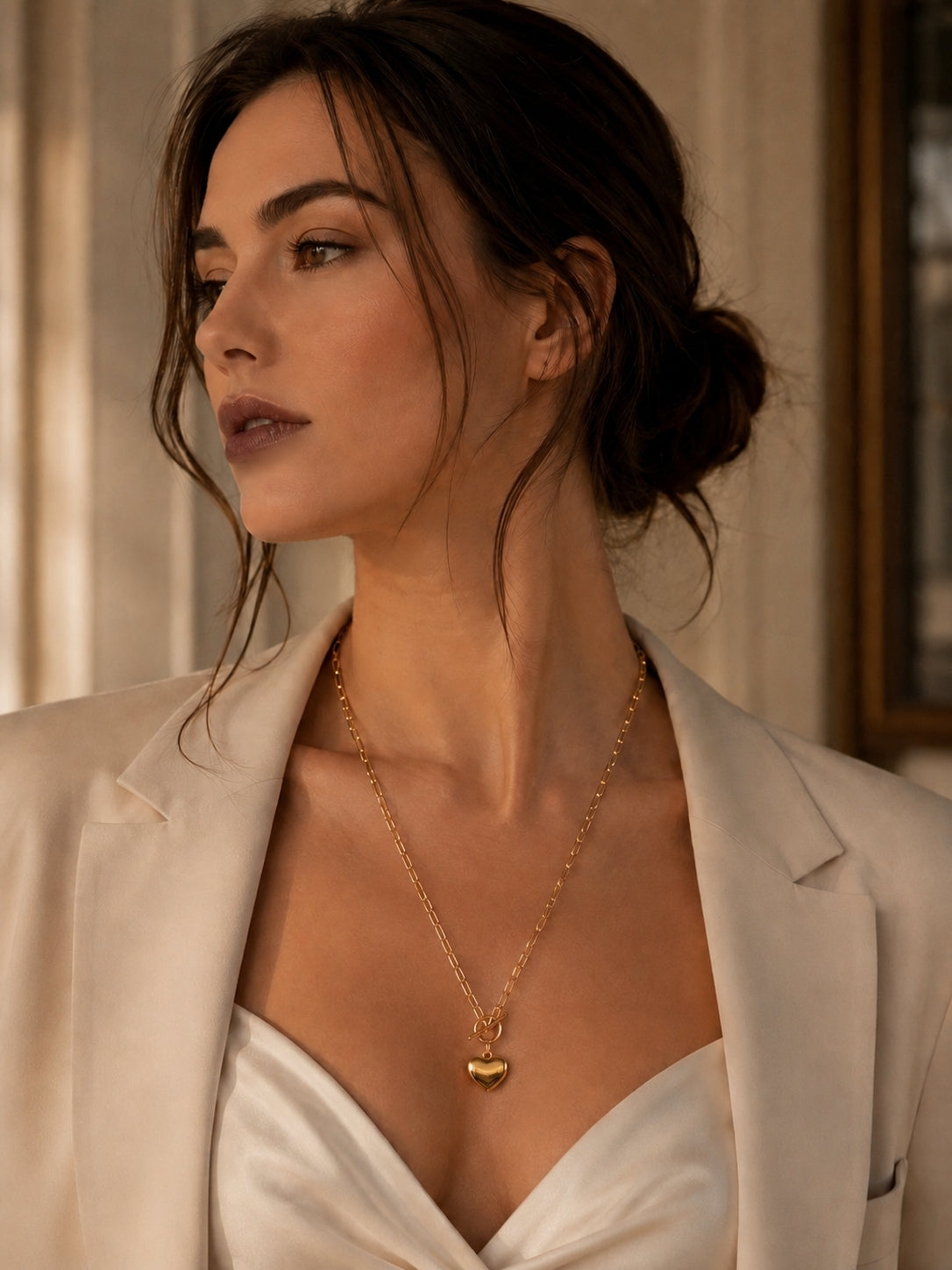 Woman wearing gold heart pendant toggle necklace with an elegant cream outfit