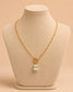 A gold chain necklace with a clear rectangular gemstone pendant, displayed on a beige jewelry bust against a warm beige background.