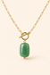 A gold chain necklace with a toggle clasp and a polished green stone pendant, shown against a solid light beige background.