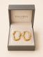 A pair of gold hoop earrings displayed inside an open gray Valoria London jewelry box on a warm cream background.