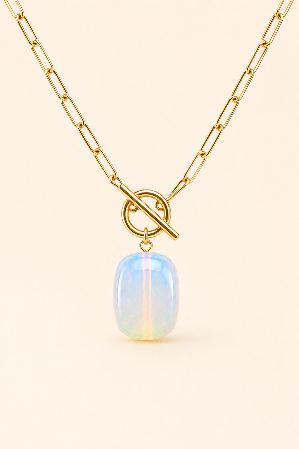 Gold chain necklace with a toggle clasp and a smooth, oval-shaped iridescent opal pendant, displayed on a light cream background.