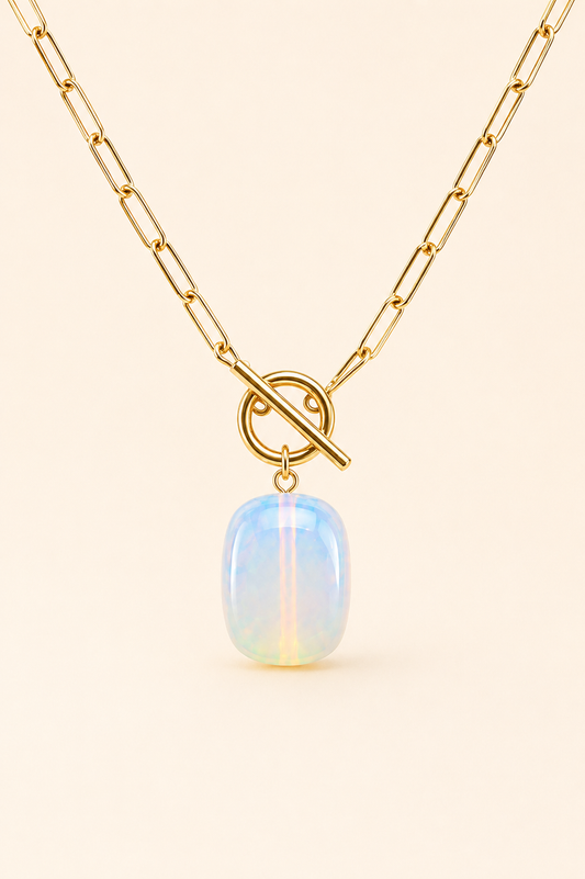 Gold chain necklace with a toggle clasp and a smooth, oval-shaped iridescent opal pendant, displayed on a light cream background.