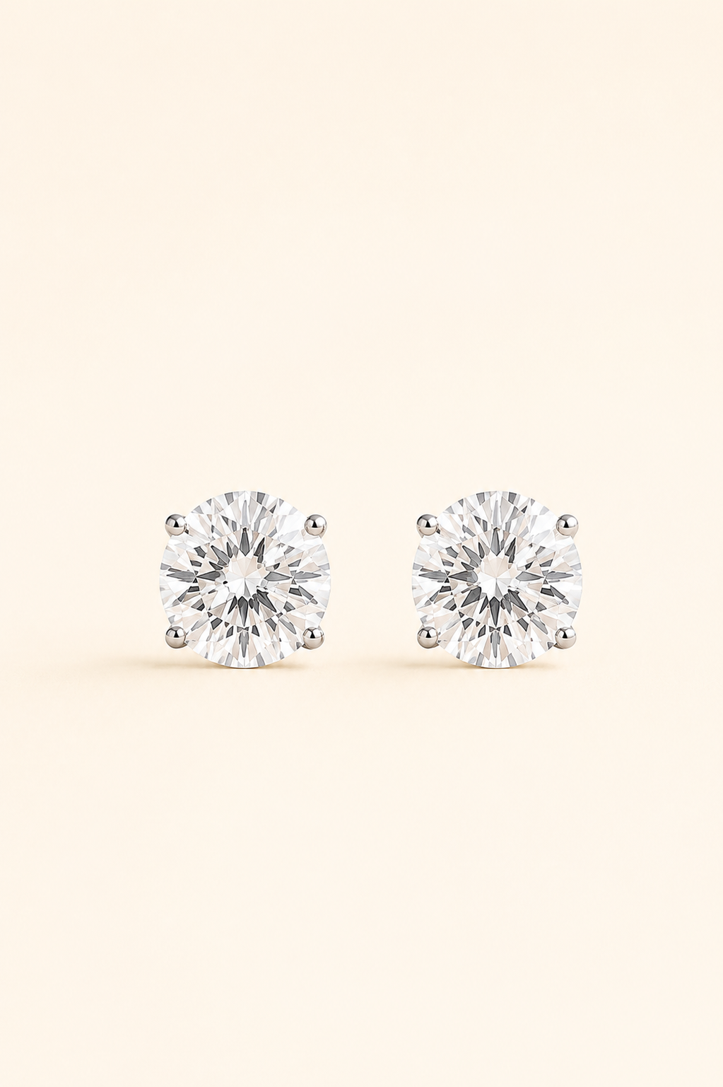 A pair of round-cut stud earrings with clear gemstones in a silver-toned prong setting, displayed on a light cream background.