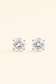 A pair of round-cut stud earrings with clear gemstones in a silver-toned prong setting, displayed on a light cream background.