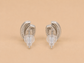 A pair of silver-toned crescent-shaped stud earrings with textured inner bands and clear plastic display tips, shown on a solid beige background.