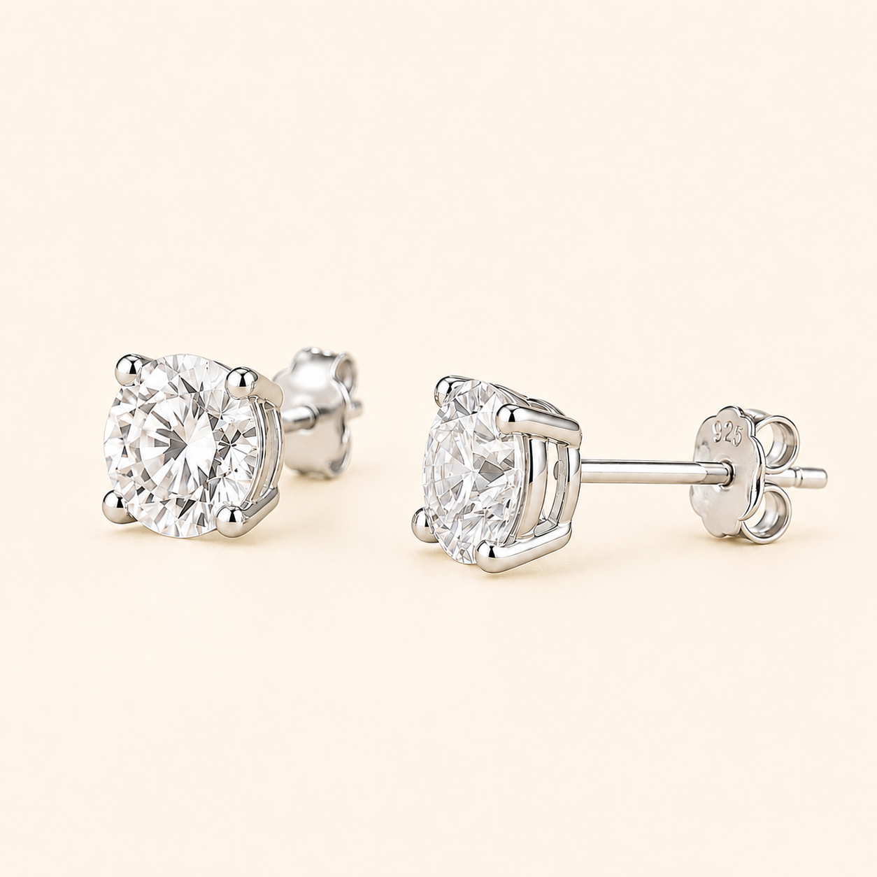 A pair of round-cut diamond stud earrings in a silver four-prong setting, shown from both front and side angles on a light cream background.