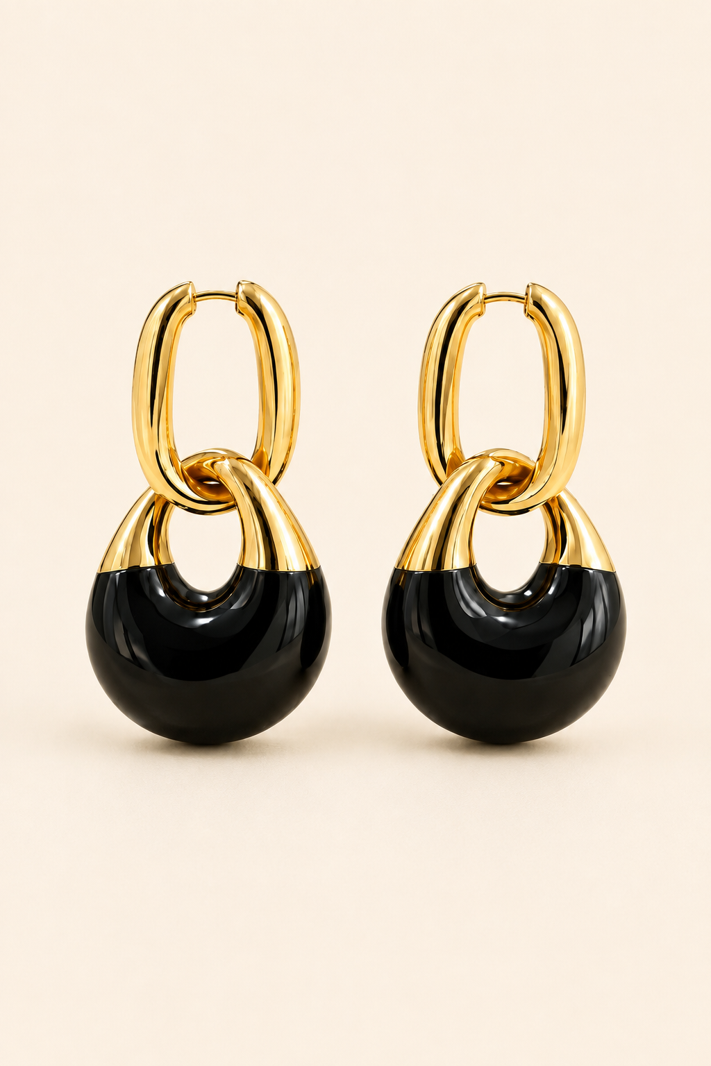 A pair of gold and black hoop drop earrings on a light beige background.