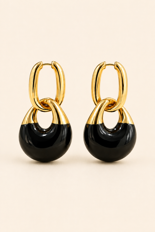 A pair of gold and black hoop drop earrings on a light beige background.