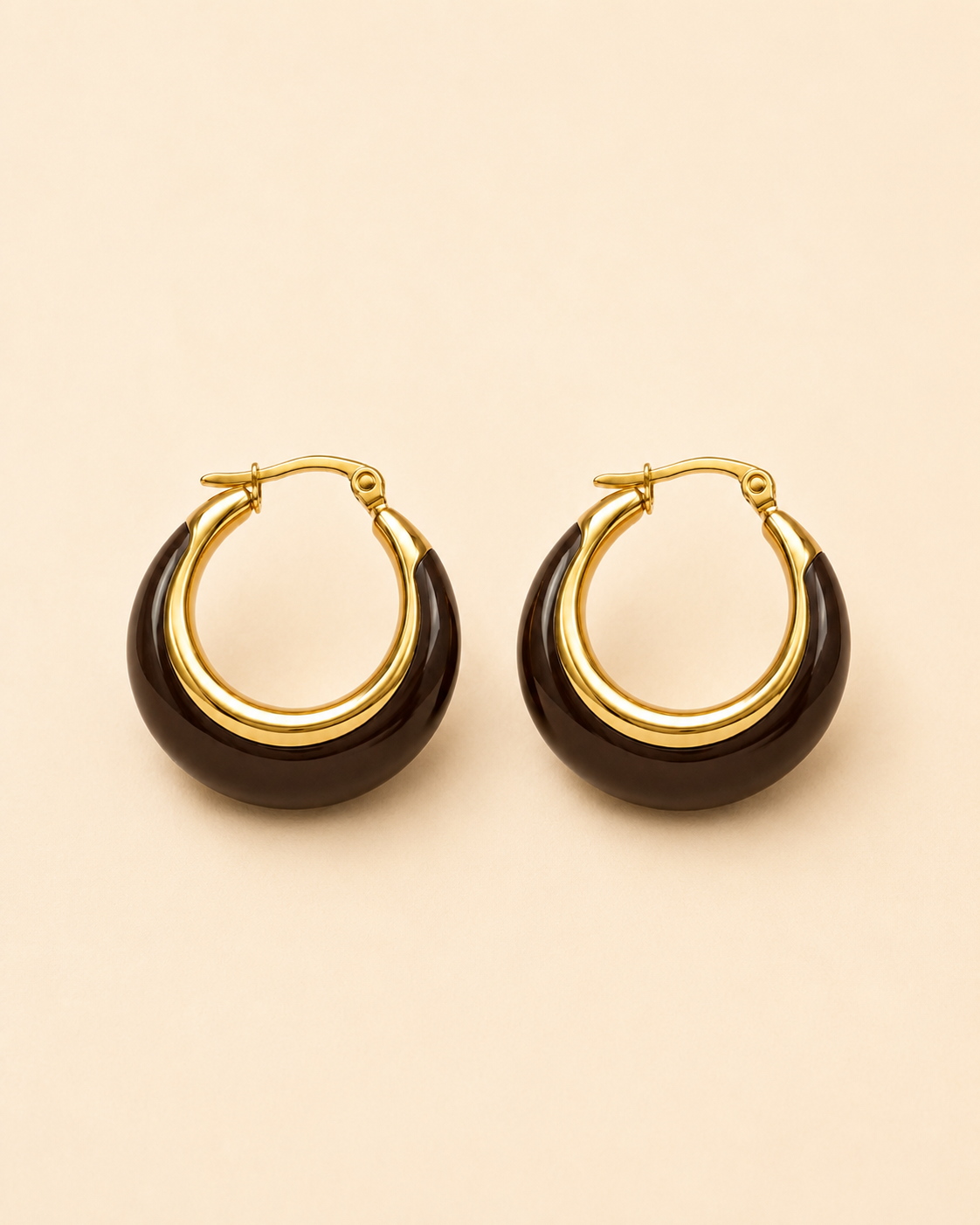 A pair of gold hoop earrings with a dark brown crescent-shaped inlay, displayed on a solid light beige background.