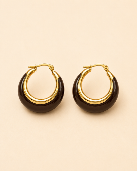 A pair of gold hoop earrings with a dark brown crescent-shaped inlay, displayed on a solid light beige background.