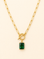 A gold paperclip chain necklace with a toggle clasp and a rectangular emerald-cut green gemstone pendant, shown on a light cream background.