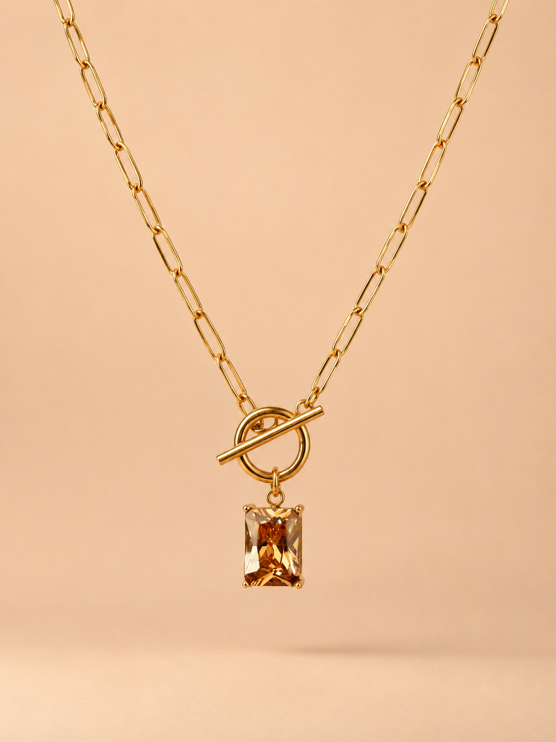 Close-up of gold toggle necklace with rectangular amber crystal pendant on a nude background