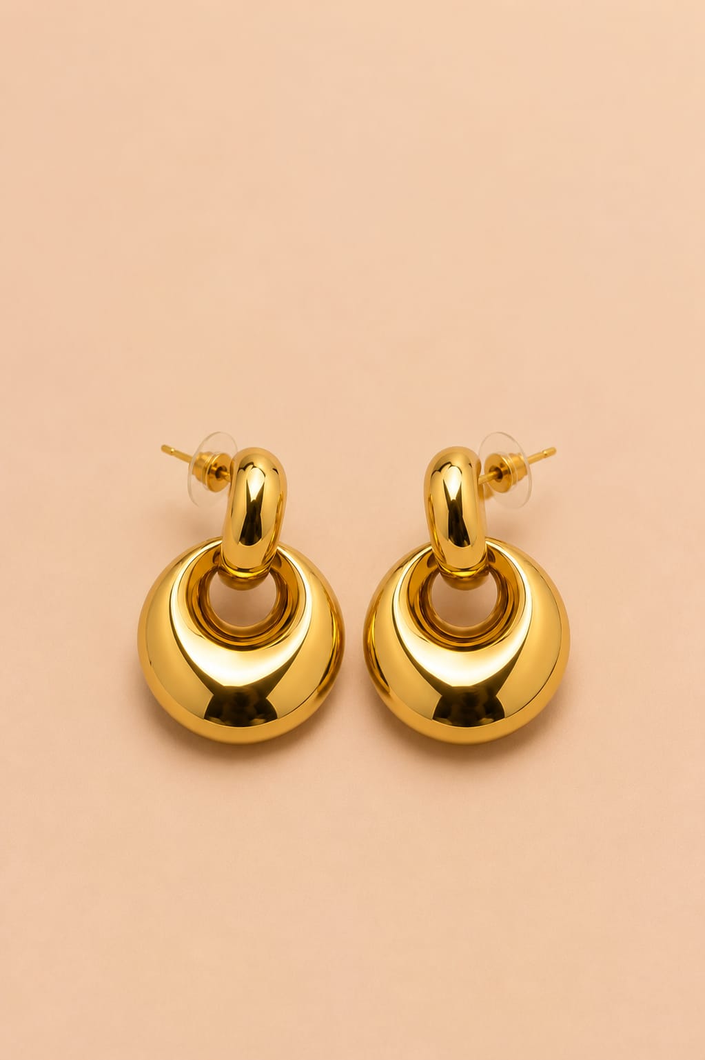 Pair of Valoria London Aurelia gold statement drop earrings displayed against a soft peach background