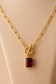 Close-up of a gold toggle necklace with a rectangular blue crystal pendant on a nude background
