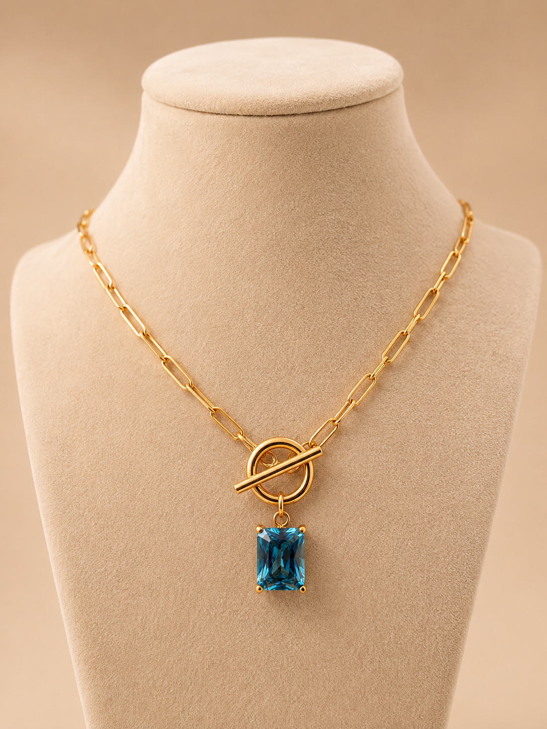Valoria London gold paperclip necklace with a rectangular blue crystal pendant displayed on a cream jewellery mannequin