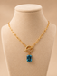 Valoria London gold paperclip necklace with a rectangular blue crystal pendant displayed on a cream jewellery mannequin