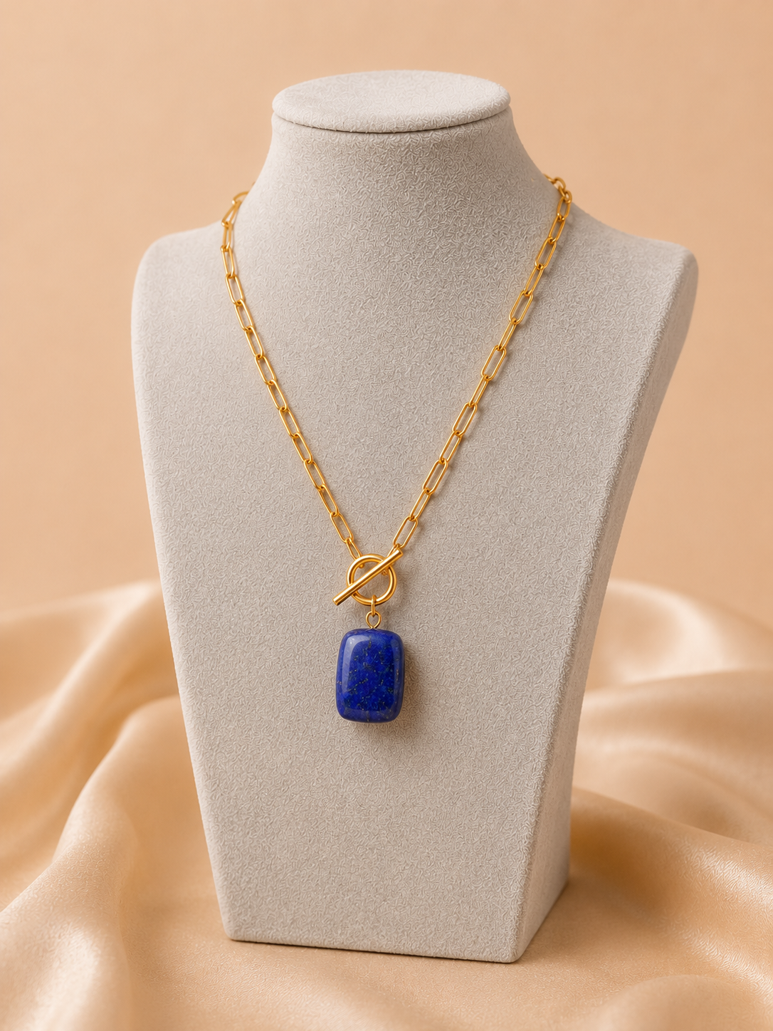 Close-up of the Valoria London Celeste gold toggle necklace featuring a polished deep blue stone pendant with gold-toned details