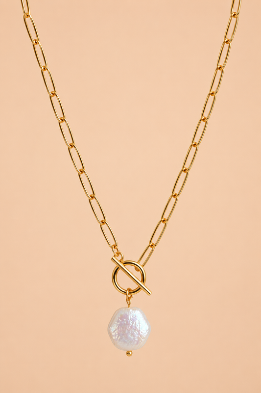 Valoria London Elara gold toggle necklace with an irregular pearl-effect pendant displayed against a soft peach background