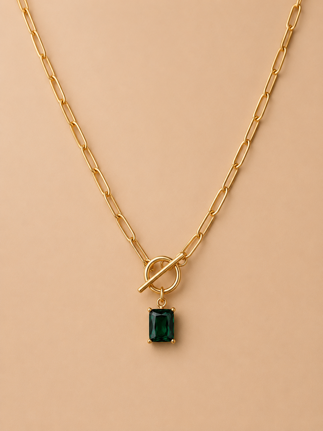 Close-up of gold toggle necklace with rectangular emerald green pendant on a nude background