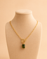 Valoria London gold paperclip necklace with emerald green pendant displayed on a cream jewellery mannequin