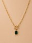 Close-up of gold toggle necklace with rectangular emerald green pendant on a nude background