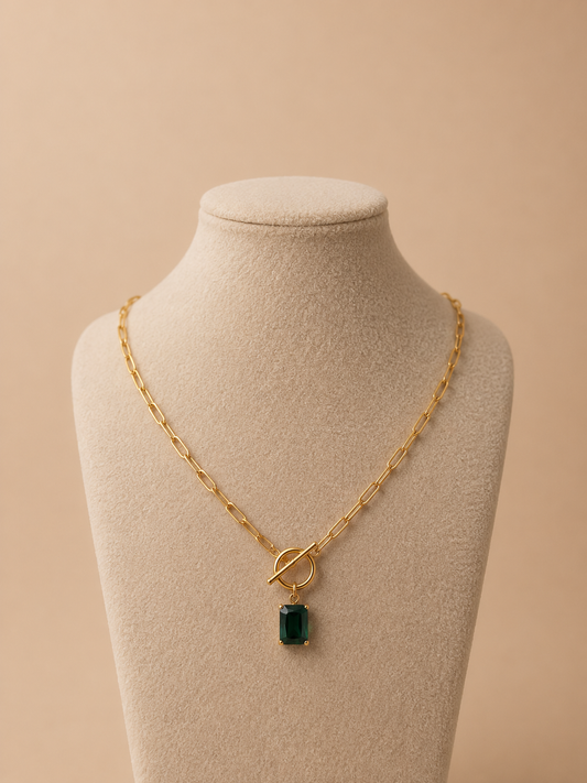 Valoria London gold paperclip necklace with emerald green pendant displayed on a cream jewellery mannequin