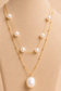 Close-up of layered gold necklace with white pearl details and a large pearl pendant