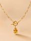 Close-up of a gold toggle necklace with a yellow teardrop crystal pendant on a nude background