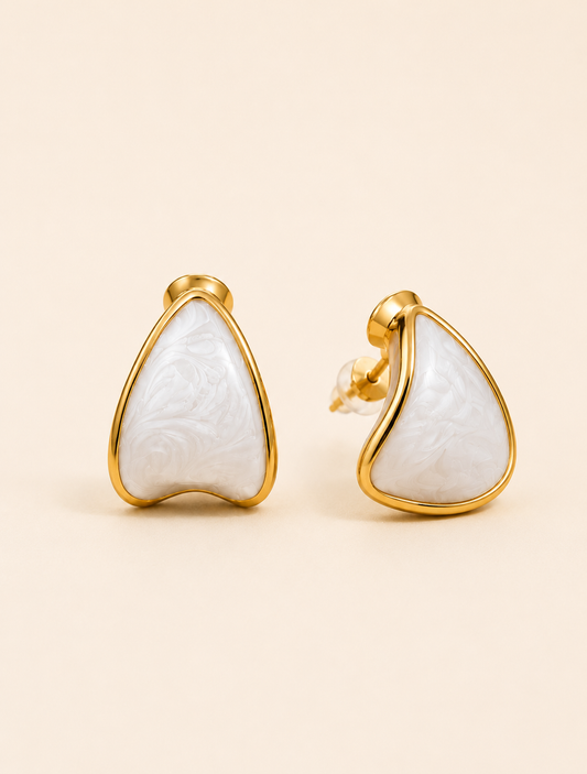 A pair of gold stud earrings with teardrop-shaped white carved stone inlays, displayed on a warm beige background.